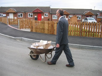 Ian Thorley dressed in suit pushing a wheel barrow around the estate with plaques and invites to creative consultation event